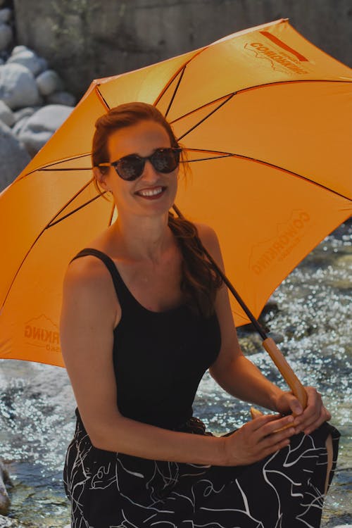 Woman in Black Tank Top Wearing Sunglasses while Holding an Orange Umbrella