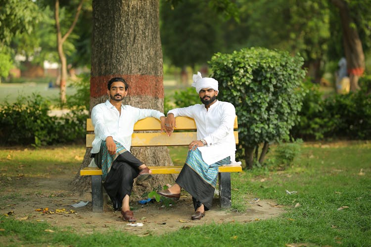 Men In Traditional Clothes Sitting On Bench In Park