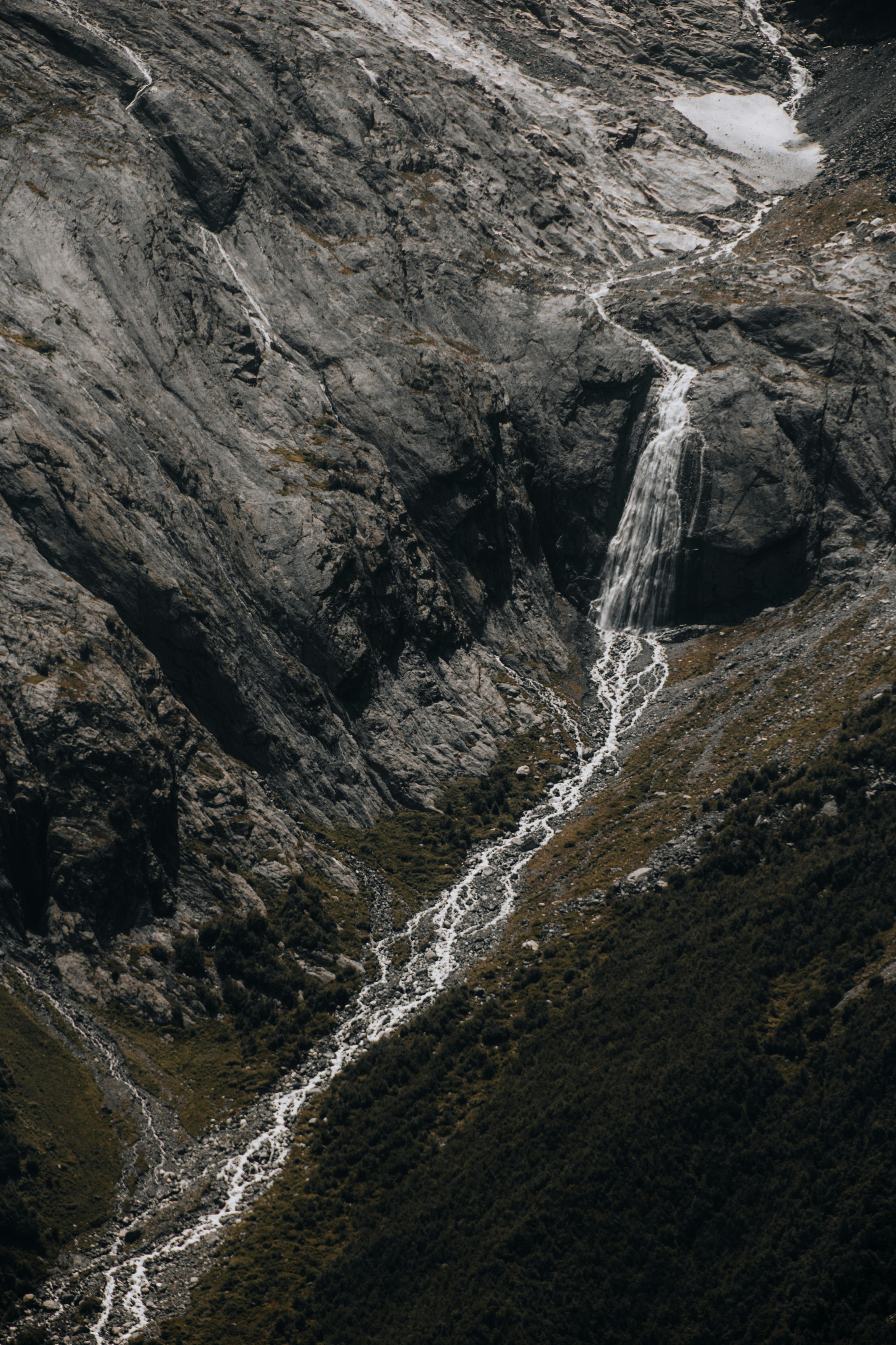 A stunning waterfall cascades down a rocky mountain landscape, creating a serene stream below.
