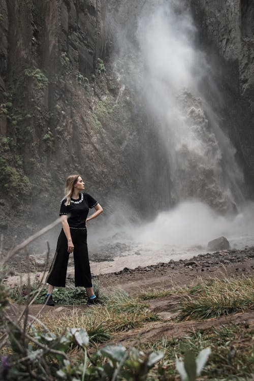 Woman Wearing Black Shirt and Pants Standing Near a Waterfalls