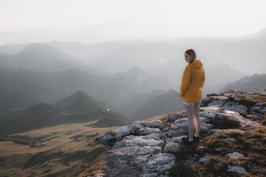 Woman standing on a rocky mountain observing a vast scenic landscape under daylight.