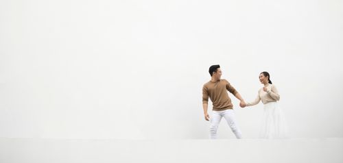 Free A happy couple holding hands and looking at each other against a minimalist white background. Stock Photo