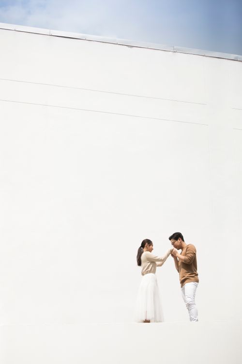 Free A loving Asian couple holding hands against a minimalistic white wall, representing love and connection. Stock Photo