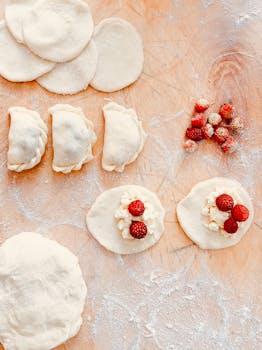 Flat lay of homemade berry-filled dumpling preparation on a floured surface.