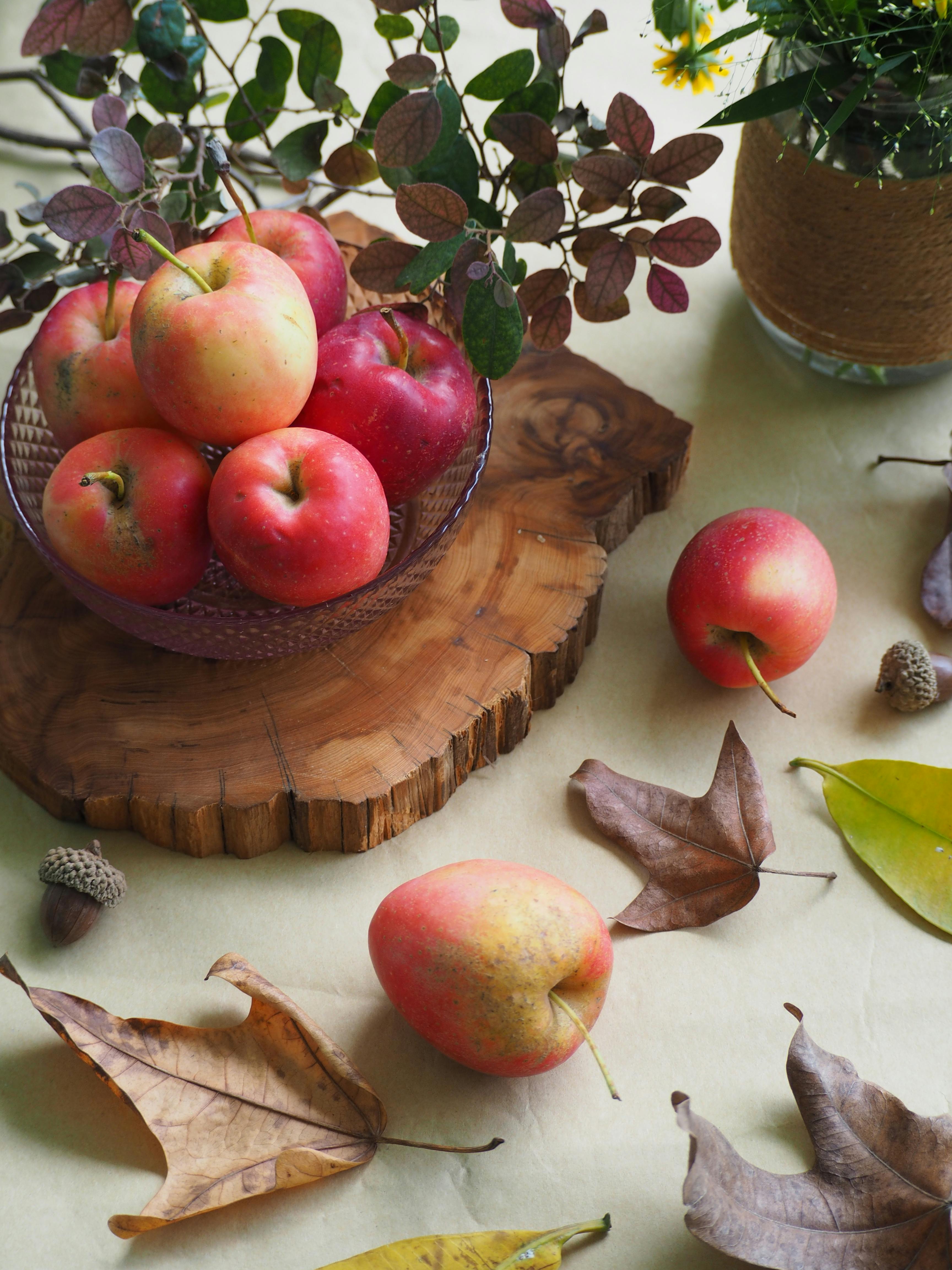 Top view of fresh apples on a wooden board with autumn leaves, embodying a cozy fall atmosphere.