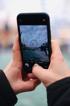 Hands holding a smartphone capturing a ferris wheel in the background.