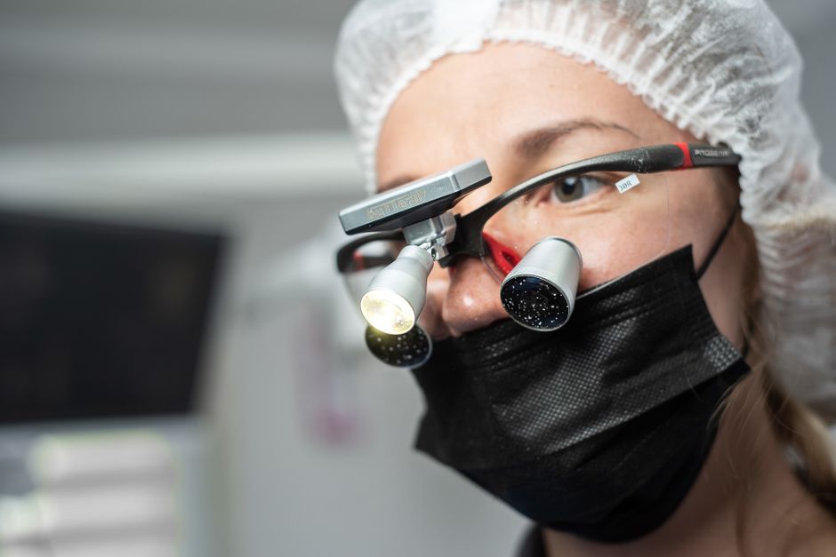 Female dentist wearing dental loupes and face mask, focused on patient care.