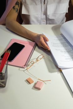 Person working at a desk with papers, phone, and pencils. Indoor office setting.