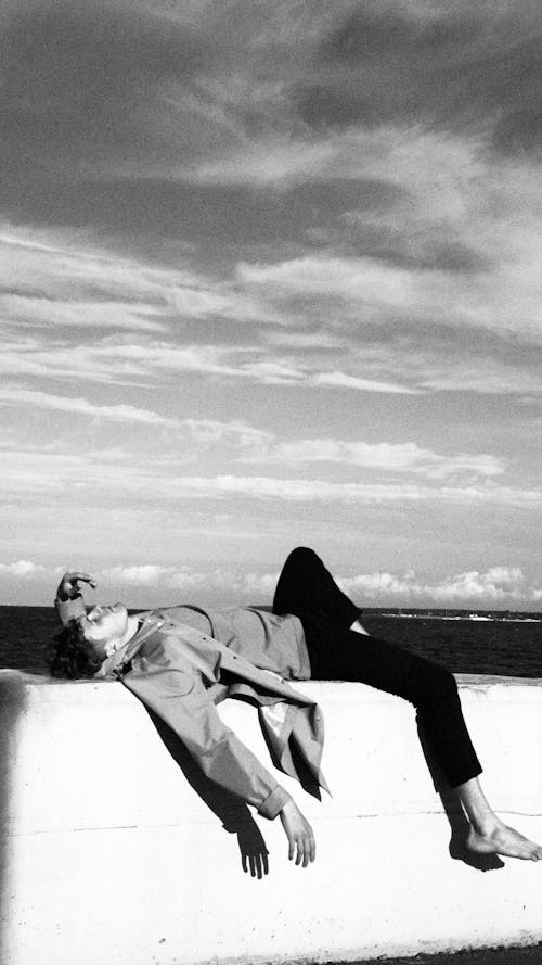 Man Lying on Concrete Fence Near Sea