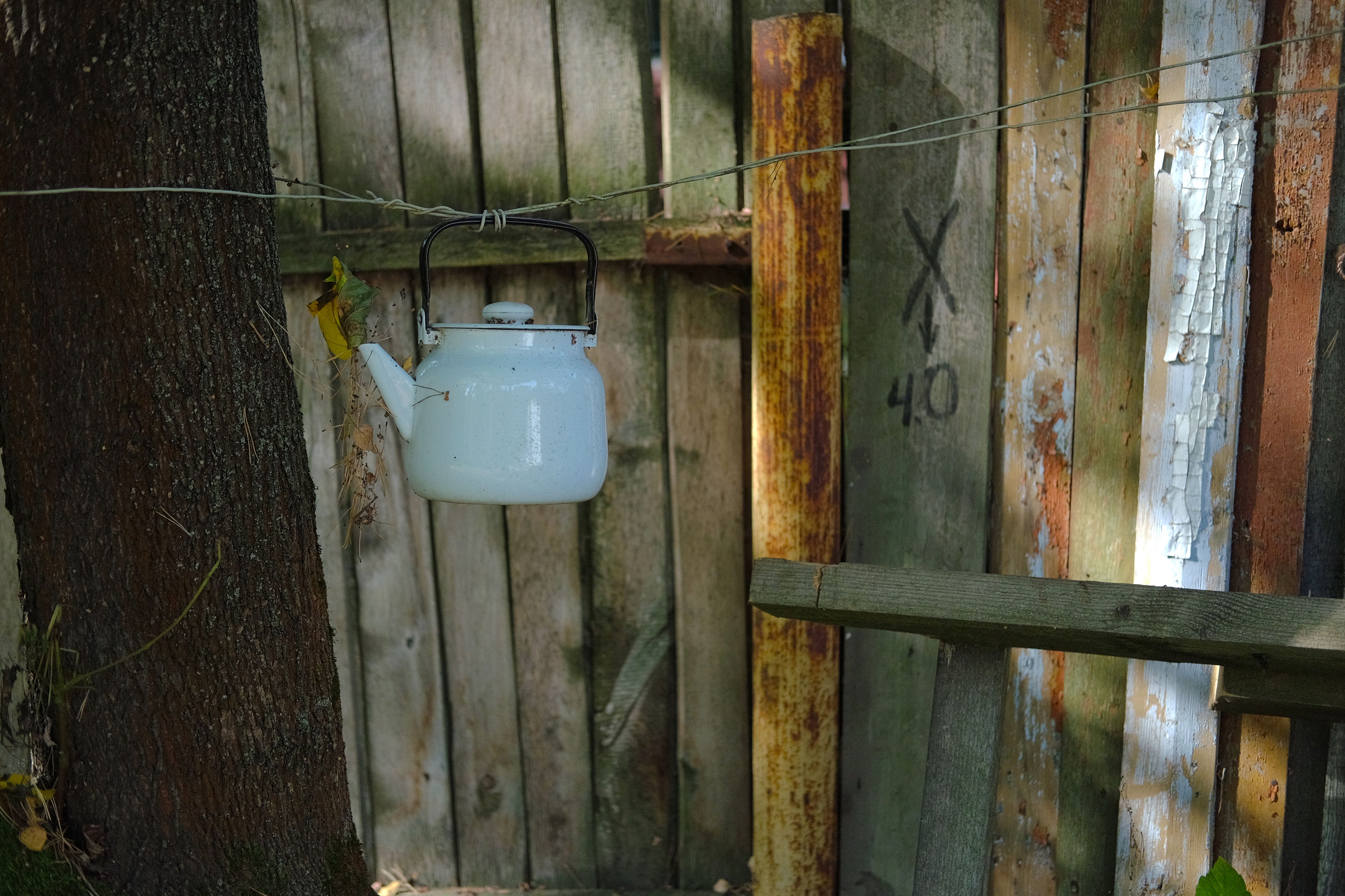 A white kettle hangs from a wire against a rustic wooden fence, showcasing a vintage outdoor aesthetic.