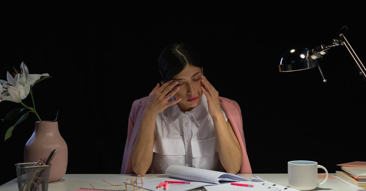 person sitting at a messy desk looking tired but smiling, 4pm sunlight streaming through window