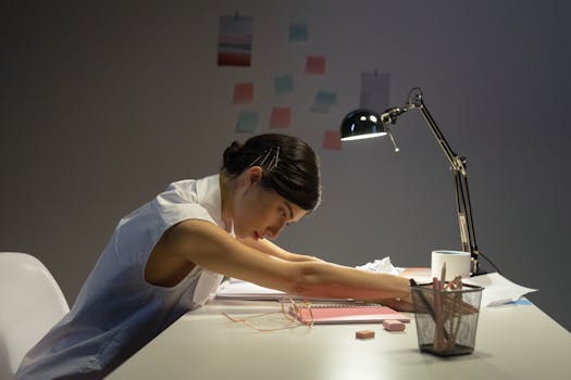 Tired young woman resting at her desk in a dimly lit office environment.
