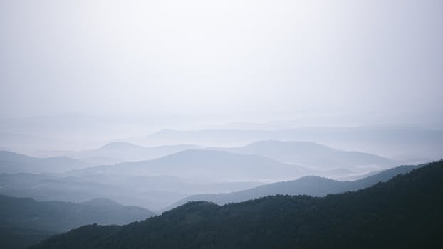 Tranquil view of misty mountain ranges under a pale sky, evoking peace and serenity.