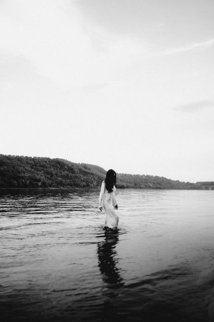 A serene black and white image of a woman walking through calm waters, capturing tranquility and solitude.
