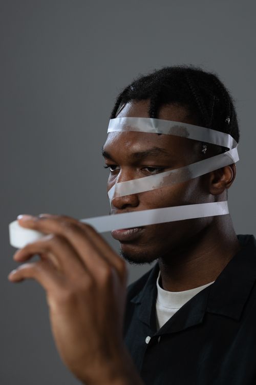 Free Artistic portrait of a man with adhesive tape wrapped around his face depicting a conceptual theme. Stock Photo