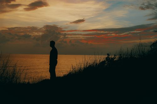 Free Silhouette of a person by the seaside during sunset with a dramatic sky, invoking tranquility and contemplation. Stock Photo