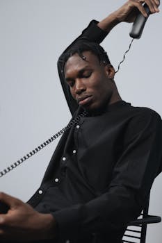 Man in black shirt holding a telephone receiver with eyes closed in a studio setting.