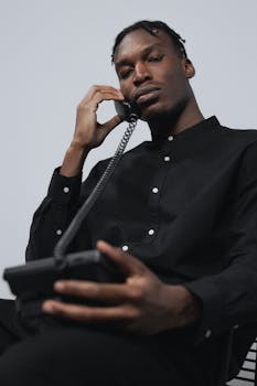 Portrait of a man in black attire talking on a vintage corded phone indoors.