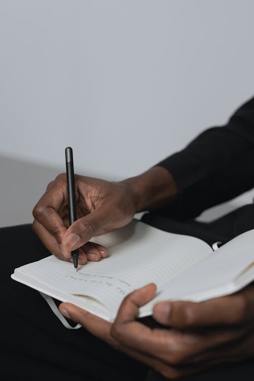 Selective Focus Photo of a Person's Hands Writing on a Notebook