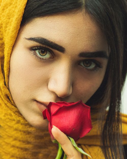 Free Close-up portrait of a woman in a yellow hijab holding a red rose. Stock Photo
