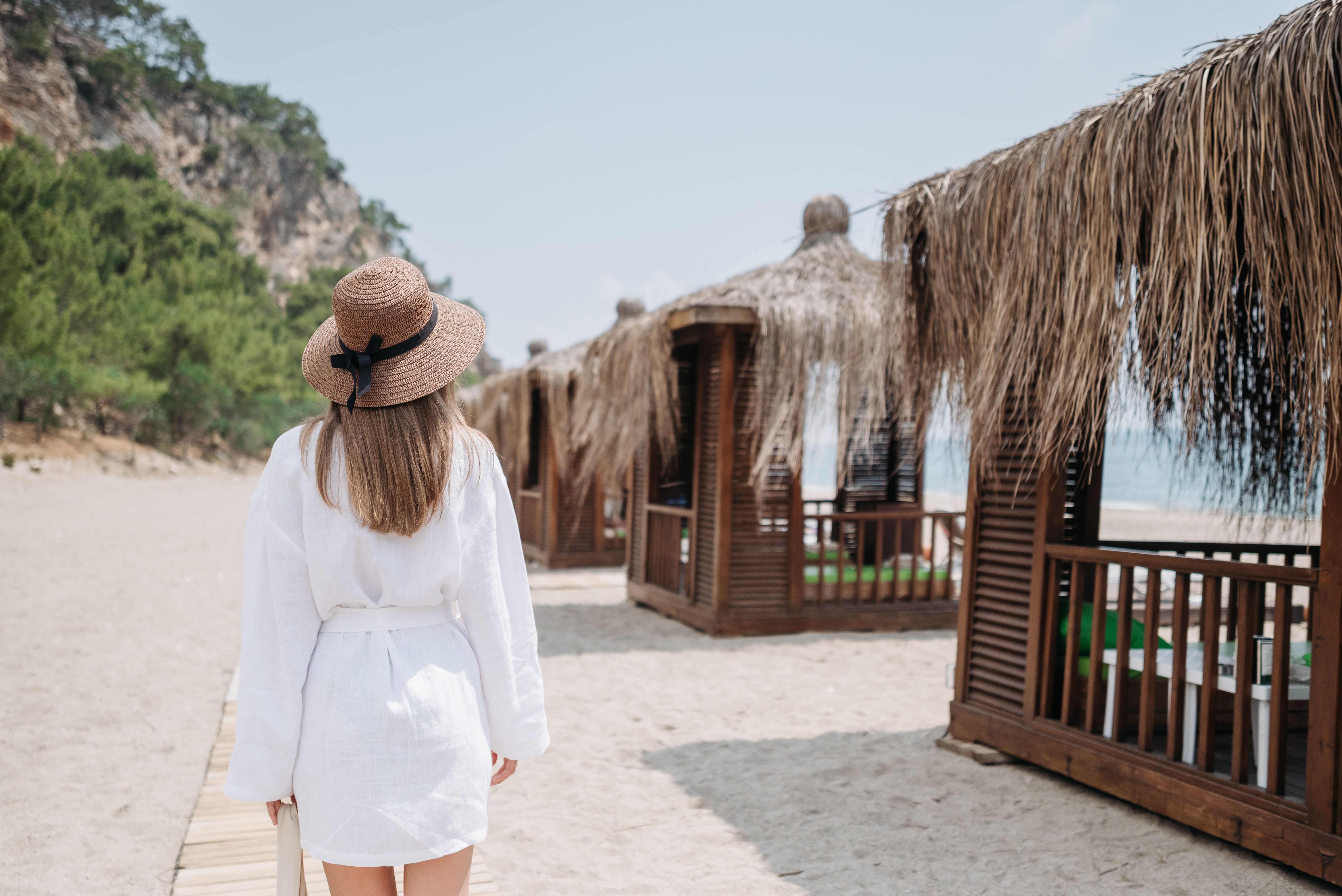 A woman in a sunhat walks along beach huts on a sunny day, enjoying a vacation atmosphere