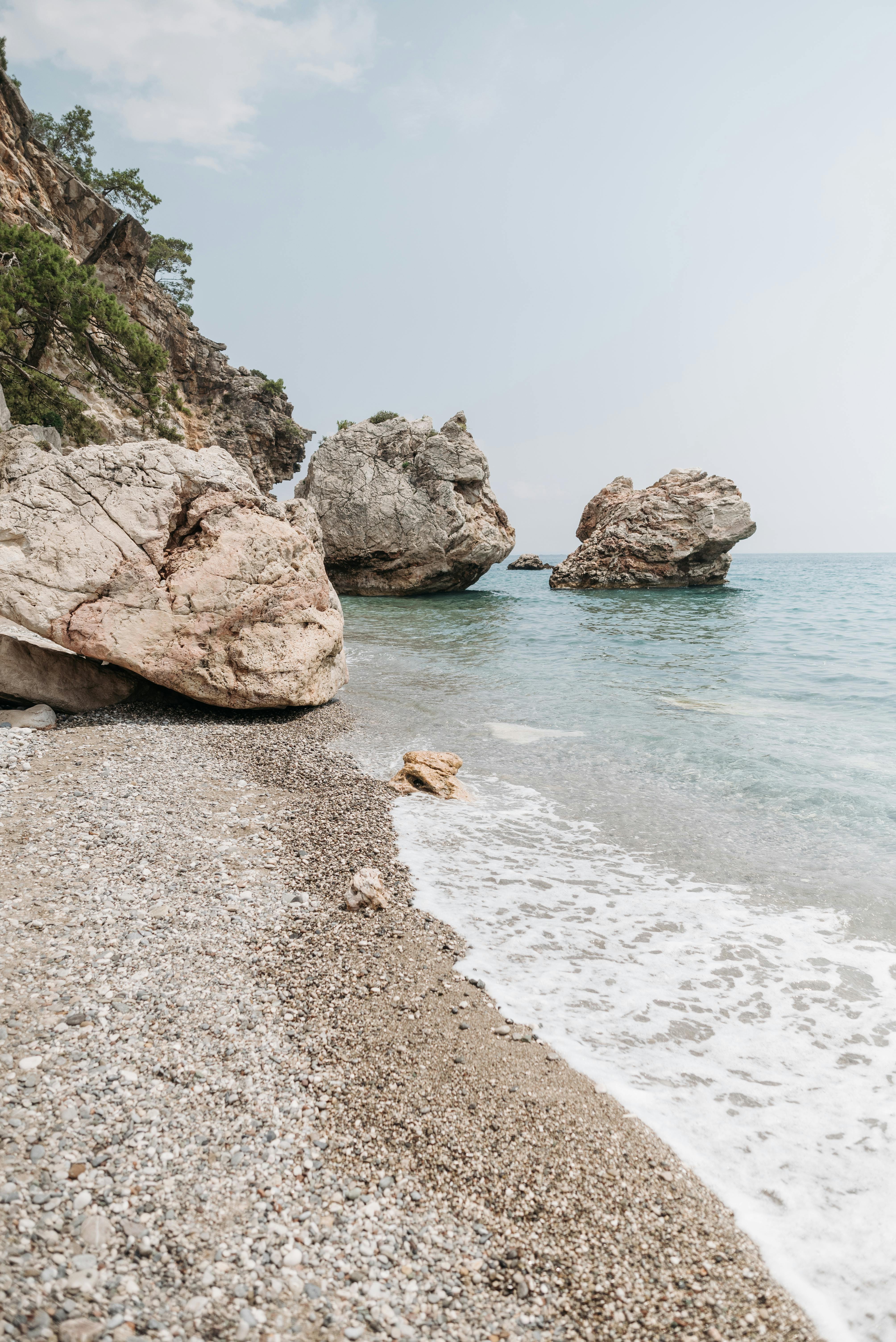 Calm seashore with stunning rock formations under a clear sky, ideal for serene vacations.