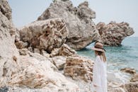 一个戴着帽子的女人站在岩石海滩旁，在夏日享受宁静的海景