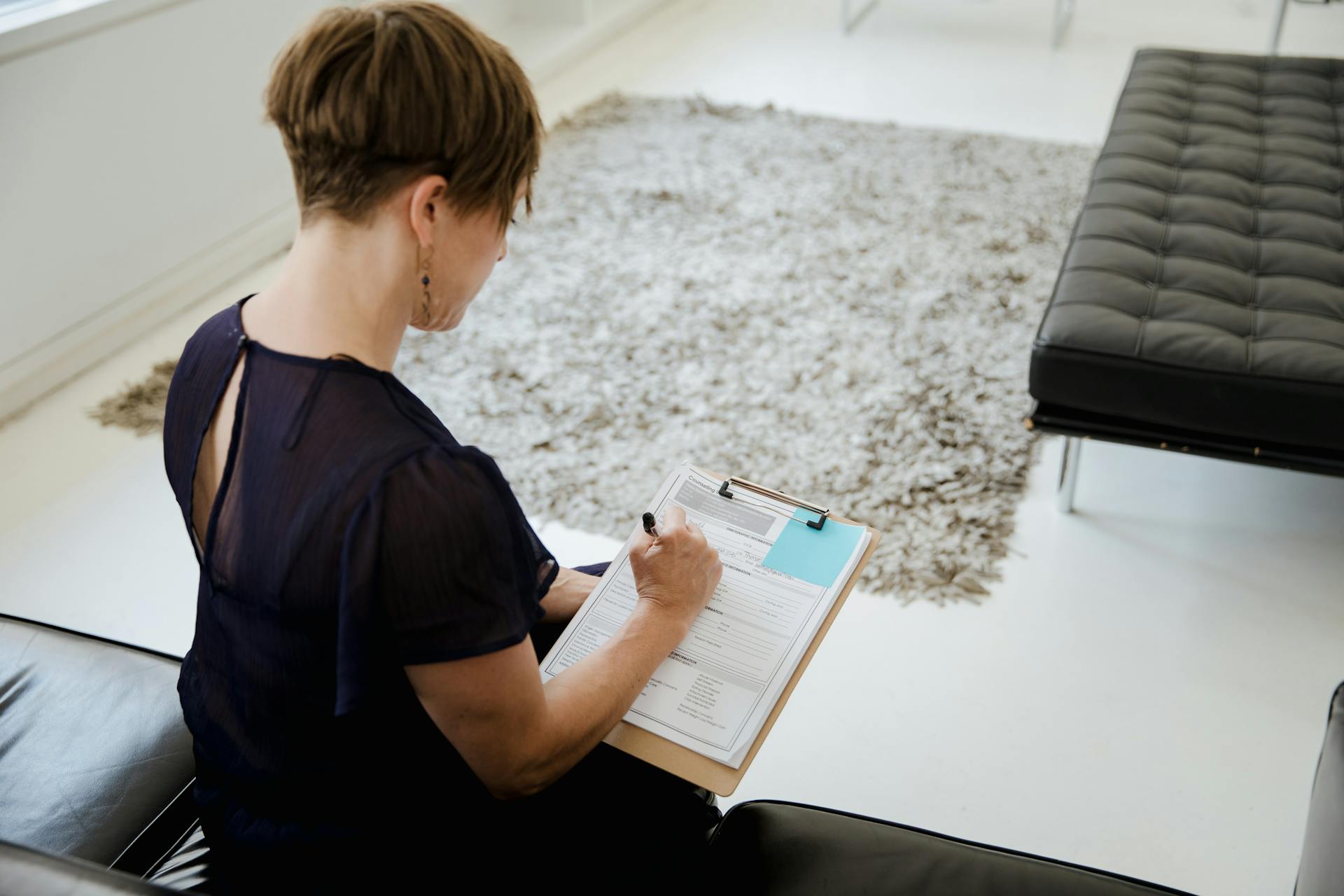 A woman sitting indoors writing on a clipboard, focused on completing paperwork.