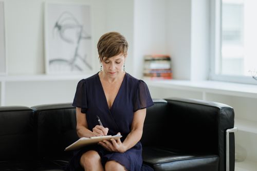 Free Businesswoman taking notes while sitting on a comfortable sofa in an office setting. Stock Photo