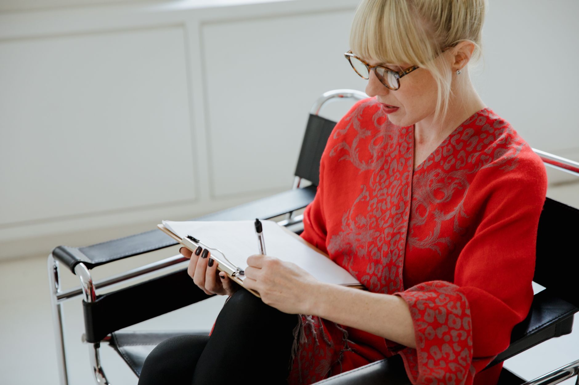 Focused adult woman in red patterned sleeves writing notes indoors.