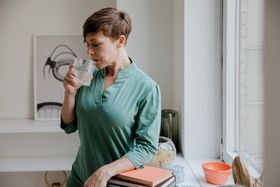 Adult woman savoring water by a window, creating a serene indoor ambiance.