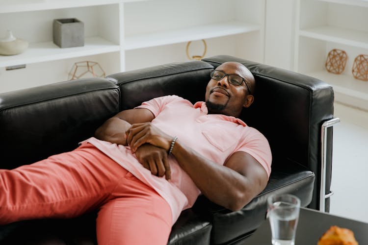 Man In Pink Polo Shirt Lying On Black Sofa