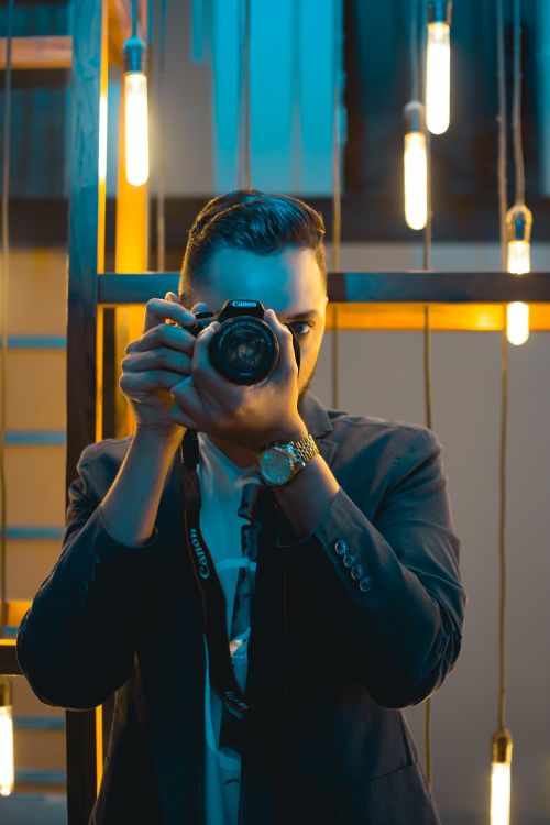 Free A stylish photographer in a modern setting capturing a shot with ambient lighting. Stock Photo