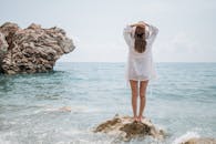 戴太阳帽的女人站在海边的岩石上，拥抱大自然的美丽