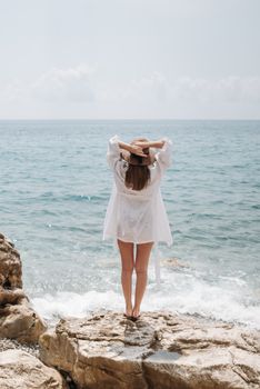 Woman standing on rocky shore in summer, gazing at the ocean under daylight.