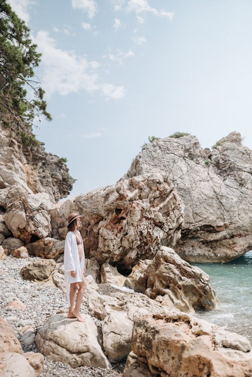 Woman in White Shirt Standing on Rocky Shore