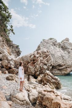 Woman standing by rocky coastline, wearing hat and swimsuit, enjoying summer by the sea.