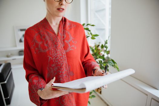Woman in red patterned shawl holding documents in well-lit modern office.