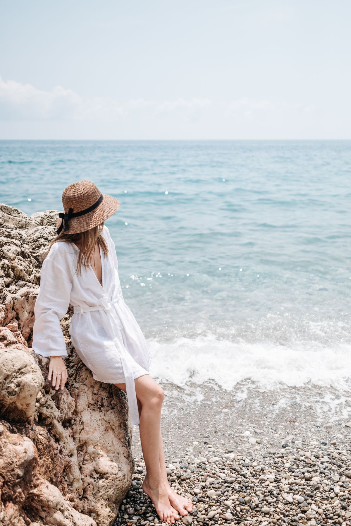 A woman in a robe leaning on a rock at the beach — the cover-up that earns its place beyond the beach