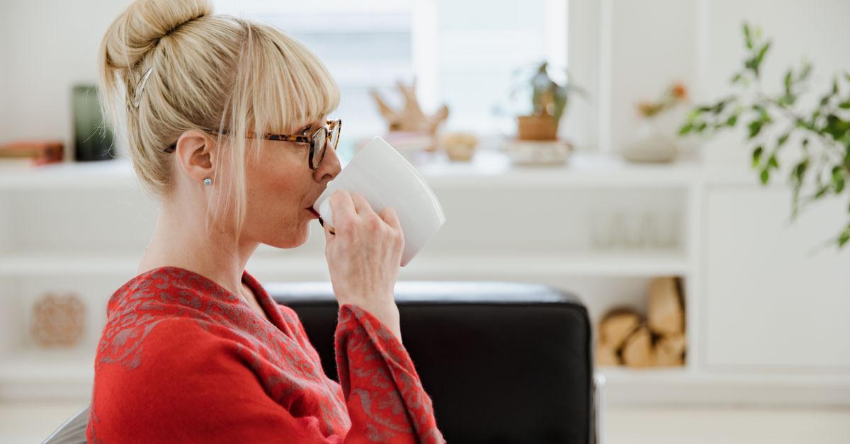 A stylish blonde woman enjoys a hot beverage in a modern and cozy living room setting.