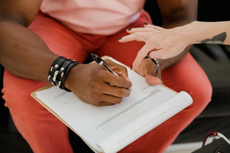 A Person Wearing Black Bracelet Filling-up  The Form On The Clipboard