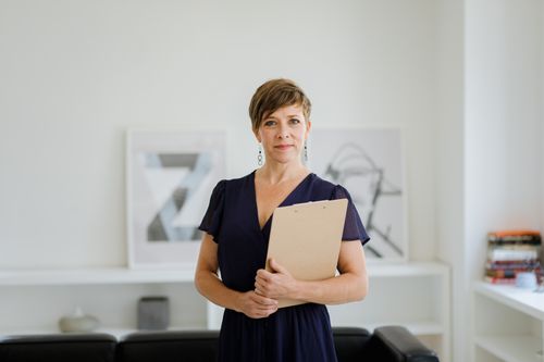Free Confident woman with short hair in office setting holding a clipboard, symbolizing professionalism. Stock Photo