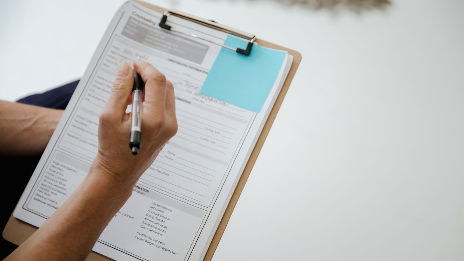 A person writes on a document using a clipboard indoors.