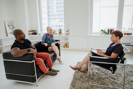 A couple in a counseling session with a therapist in a modern office setting.