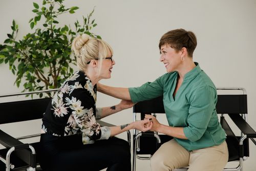 Free Two friends sitting indoors, sharing a joyful moment and supporting each other. Stock Photo