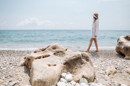 Woman in a White Shirt and Hat Walking on a Beach 