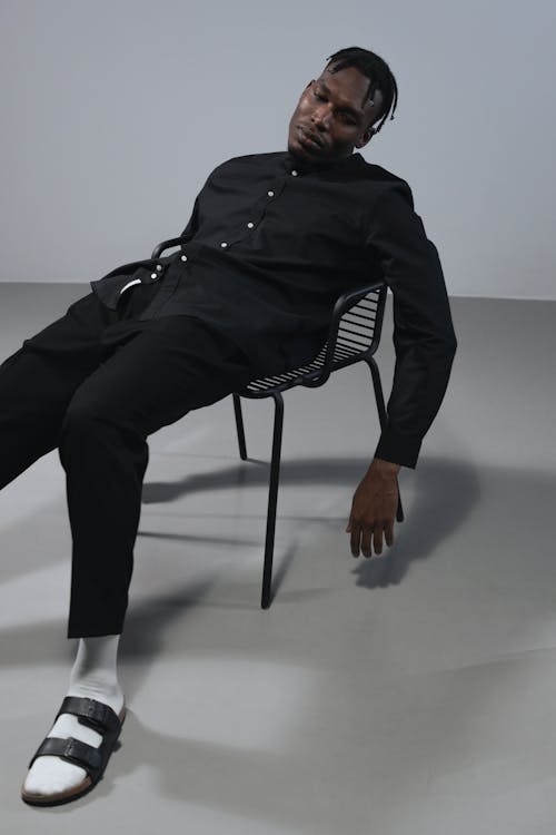 Man in Black Shirt, Pants, and Sandals Slumping in a Chair