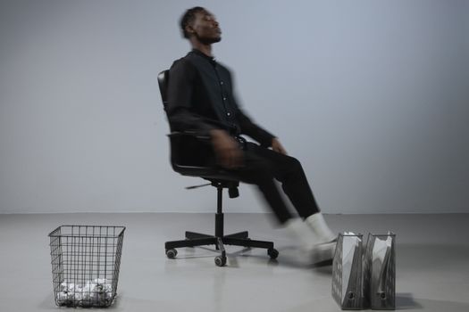 Dynamic office scene with blurred motion of man on chair, files and trash bin in focus.