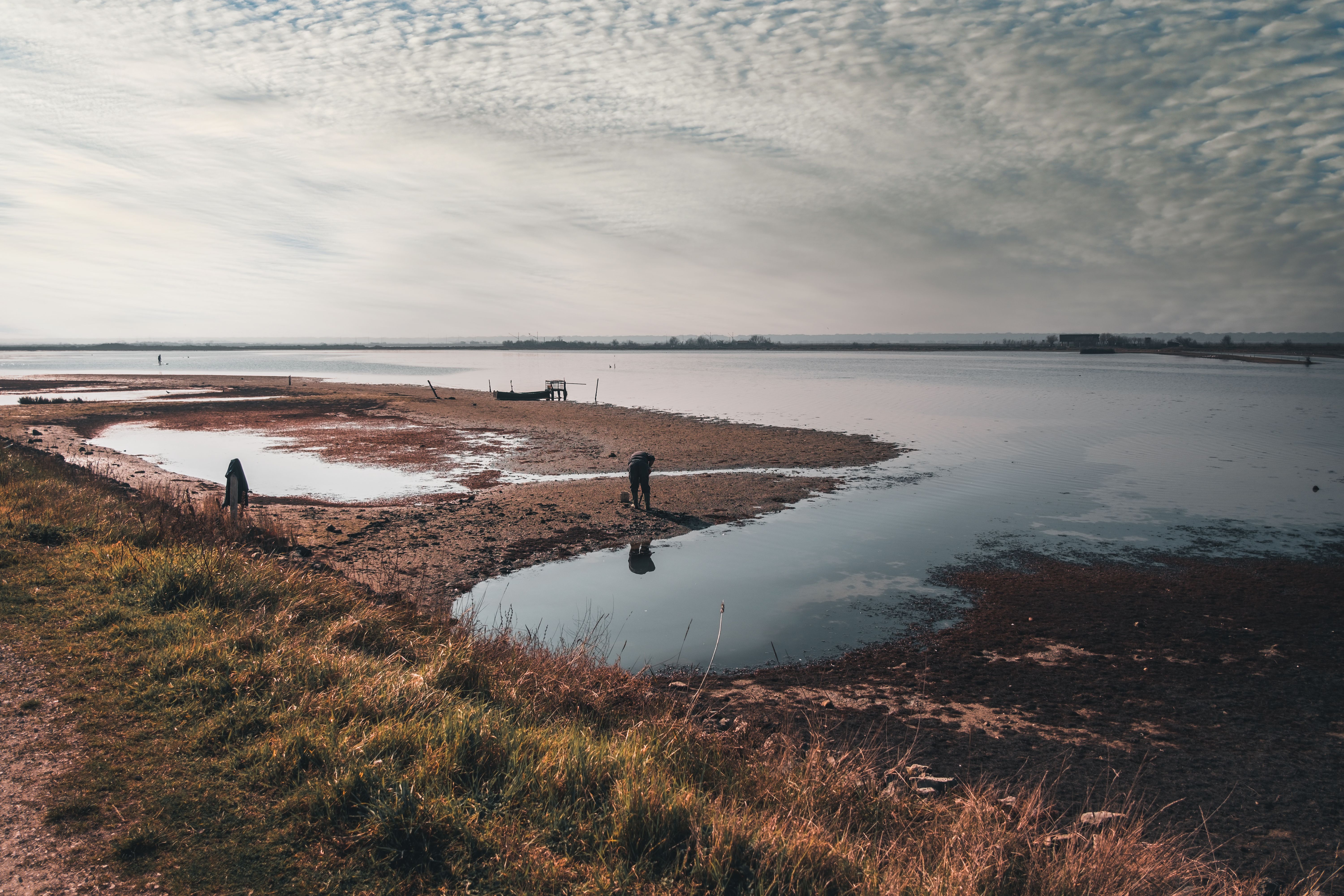 Tranquil rural scene of people by a reflective shore on a cloudy day.