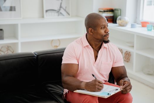 Therapist in pink shirt taking notes on clipboard, sitting in a modern office space.